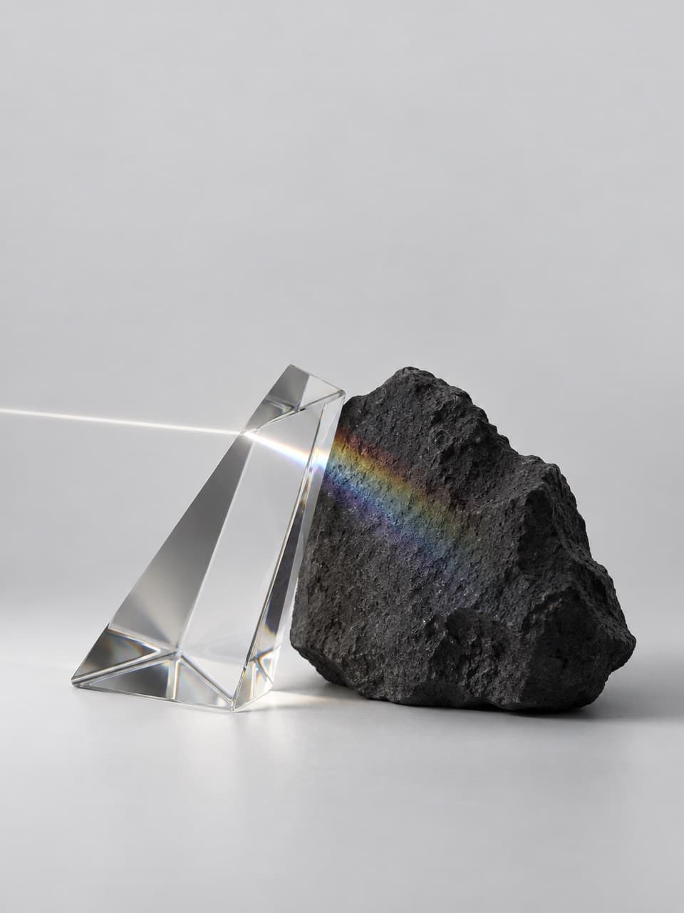 A glass prism leaning on a black stone, splitting a beam of light into a spectrum.
